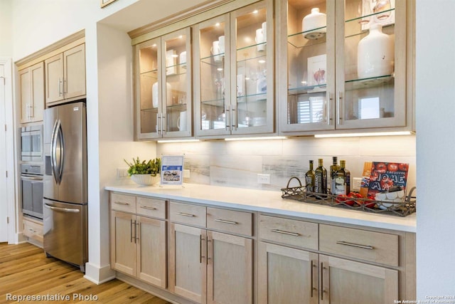 bar featuring appliances with stainless steel finishes, light hardwood / wood-style floors, and decorative backsplash