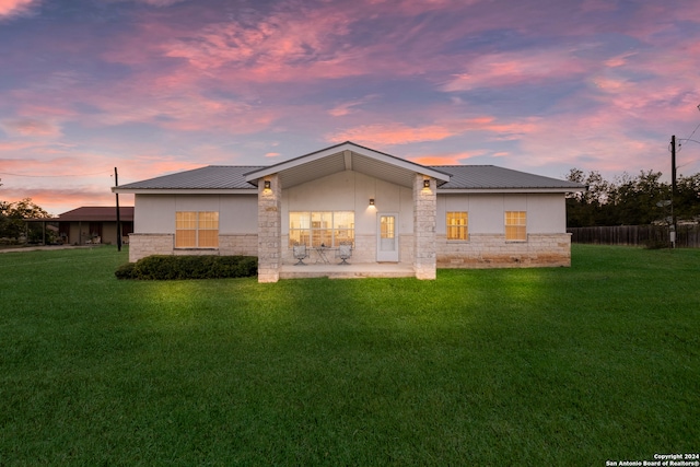 back house at dusk featuring a patio and a lawn