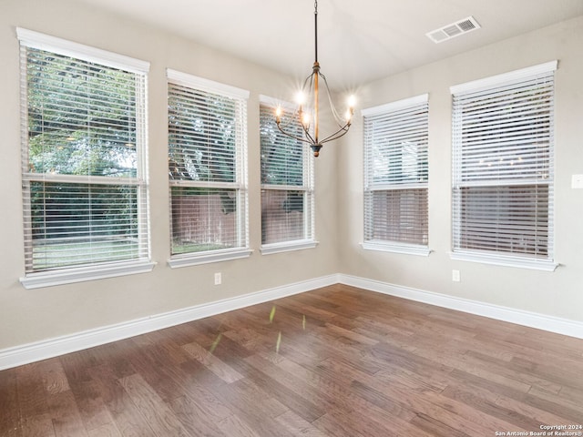 unfurnished dining area featuring an inviting chandelier, a wealth of natural light, and wood-type flooring