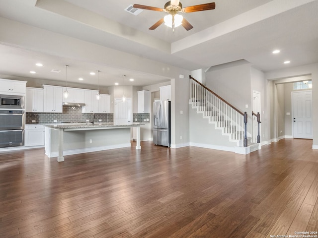 unfurnished living room with ceiling fan, a raised ceiling, and dark wood-type flooring