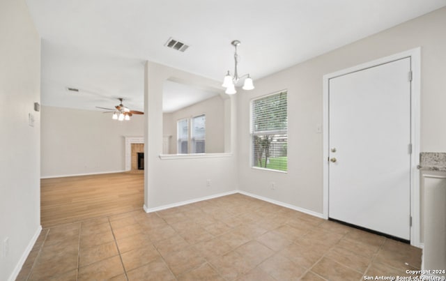 interior space featuring ceiling fan with notable chandelier, light tile patterned floors, and a brick fireplace