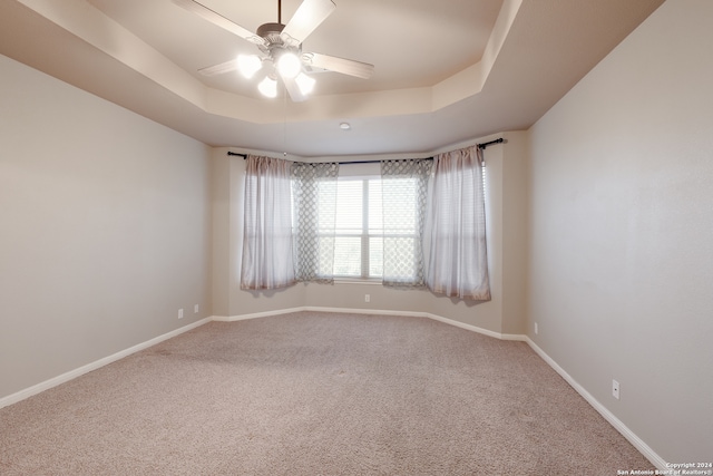 carpeted spare room with ceiling fan and a raised ceiling