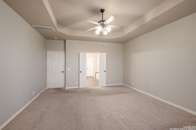 unfurnished bedroom featuring light carpet, a tray ceiling, and ceiling fan