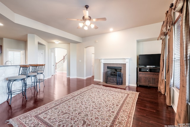 living room featuring ceiling fan, a tiled fireplace, and dark hardwood / wood-style flooring