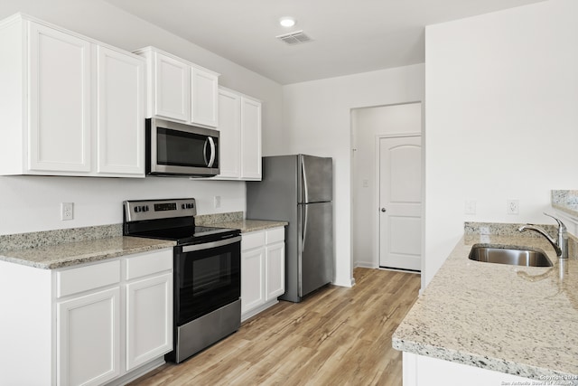 kitchen with appliances with stainless steel finishes, white cabinets, light stone countertops, light hardwood / wood-style flooring, and sink