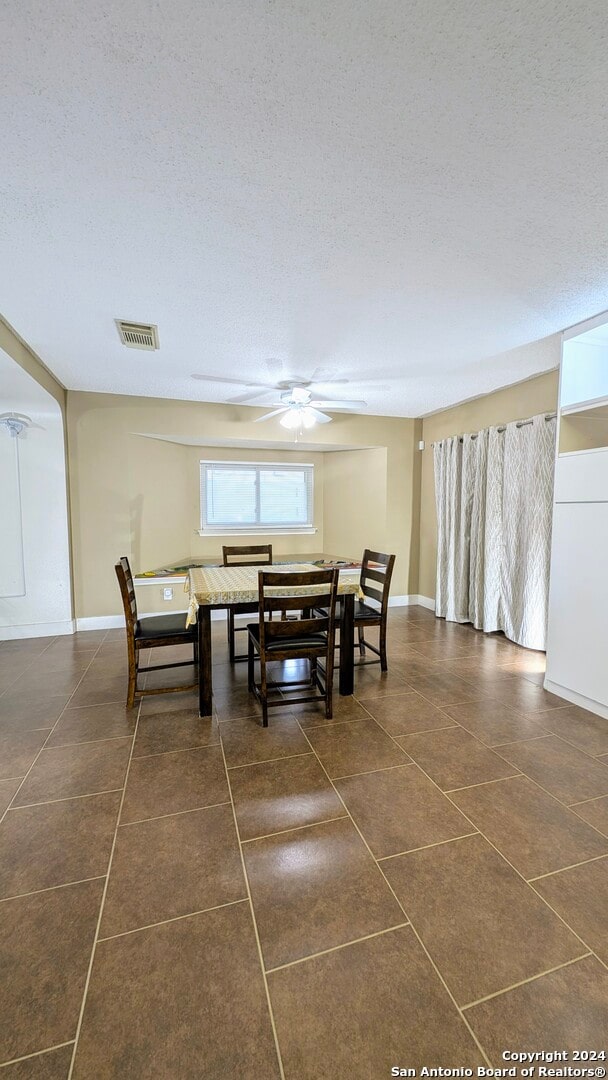 dining space featuring a textured ceiling, ceiling fan, and dark tile patterned flooring