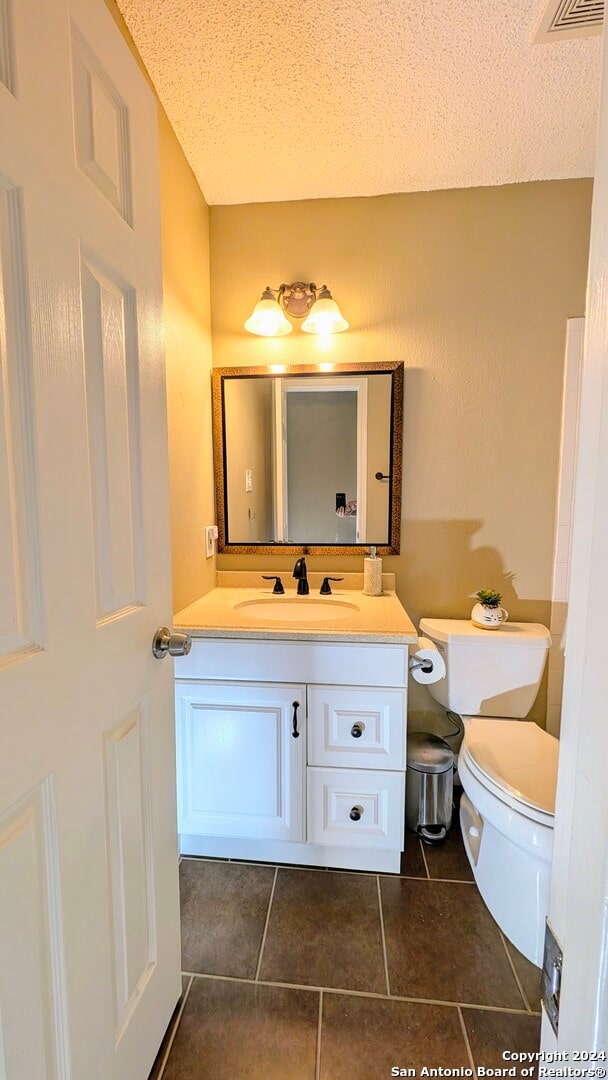 bathroom with a textured ceiling, tile patterned flooring, vanity, and toilet