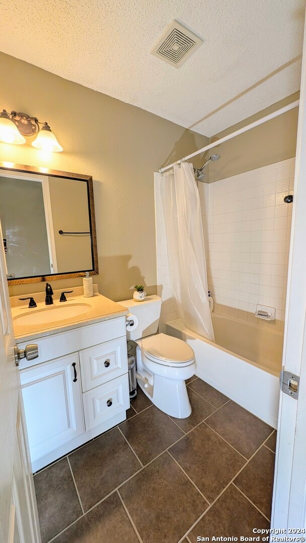 full bathroom featuring a textured ceiling, tile patterned floors, shower / tub combo with curtain, vanity, and toilet