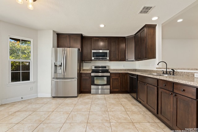 kitchen with stainless steel appliances, light tile patterned floors, sink, and light stone counters