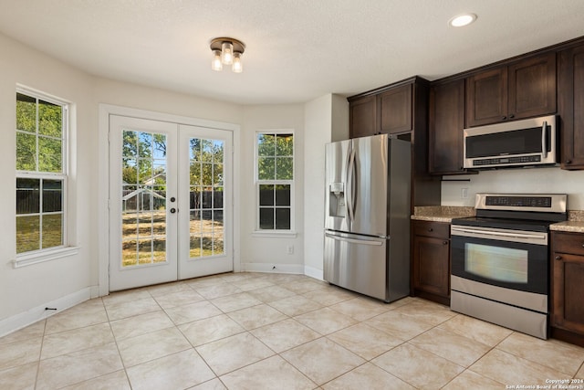 kitchen with light stone counters, light tile patterned floors, dark brown cabinets, french doors, and appliances with stainless steel finishes