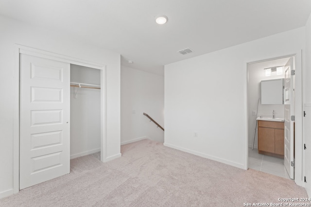 unfurnished bedroom featuring light carpet, a closet, and ensuite bath