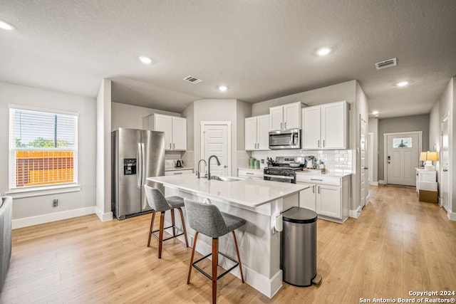 kitchen featuring white cabinets, an island with sink, sink, light hardwood / wood-style flooring, and appliances with stainless steel finishes