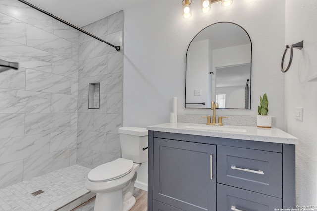 bathroom featuring hardwood / wood-style flooring, vanity, tiled shower, and toilet