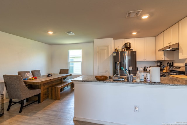 kitchen with dark stone countertops, white cabinets, kitchen peninsula, stainless steel appliances, and light hardwood / wood-style flooring