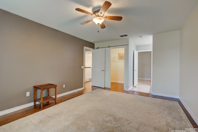 unfurnished bedroom with ceiling fan, wood-type flooring, a closet, a spacious closet, and a barn door