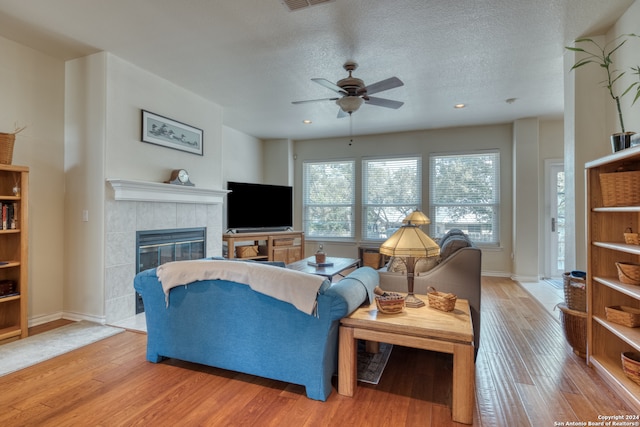 living room with ceiling fan, a textured ceiling, light hardwood / wood-style flooring, and a tiled fireplace