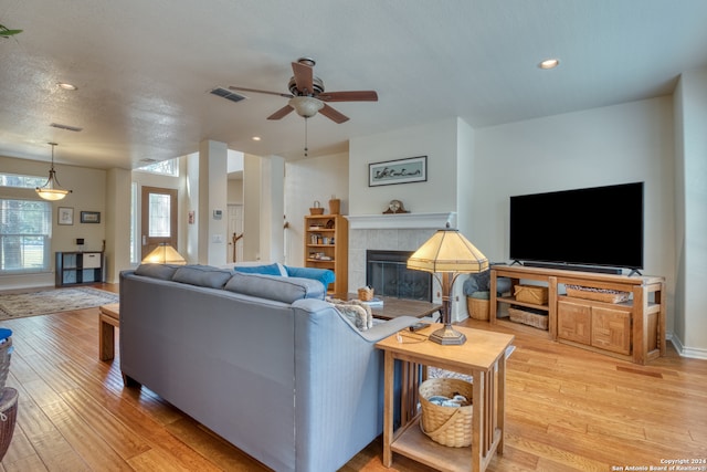 living room featuring a textured ceiling, a tile fireplace, ceiling fan, and light hardwood / wood-style flooring