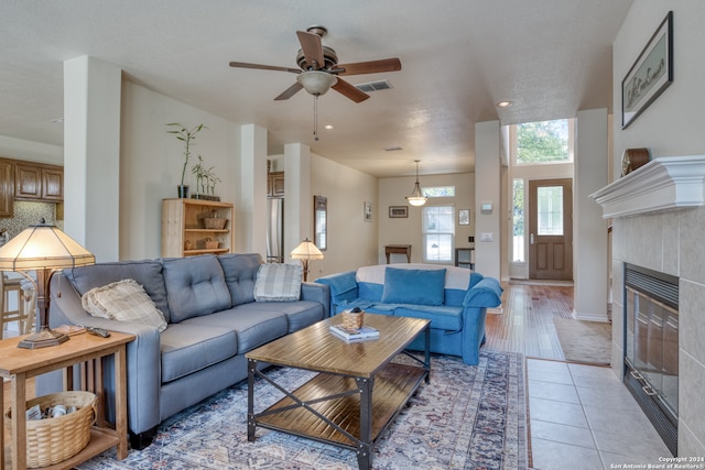 living room with ceiling fan, a textured ceiling, light hardwood / wood-style flooring, and a tile fireplace