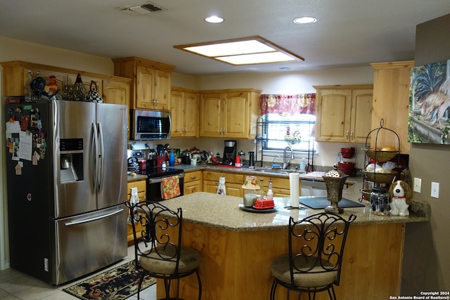 kitchen featuring sink, kitchen peninsula, a kitchen bar, appliances with stainless steel finishes, and light tile patterned floors