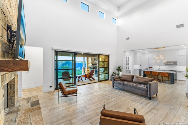 living room with a towering ceiling, light hardwood / wood-style floors, a fireplace, and sink