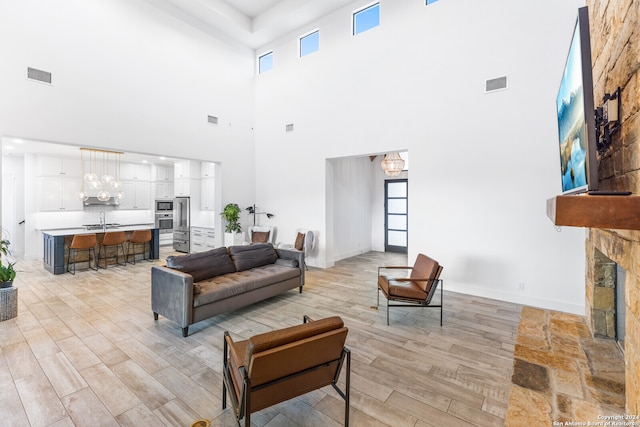 living room featuring sink, a stone fireplace, light hardwood / wood-style flooring, an inviting chandelier, and a towering ceiling