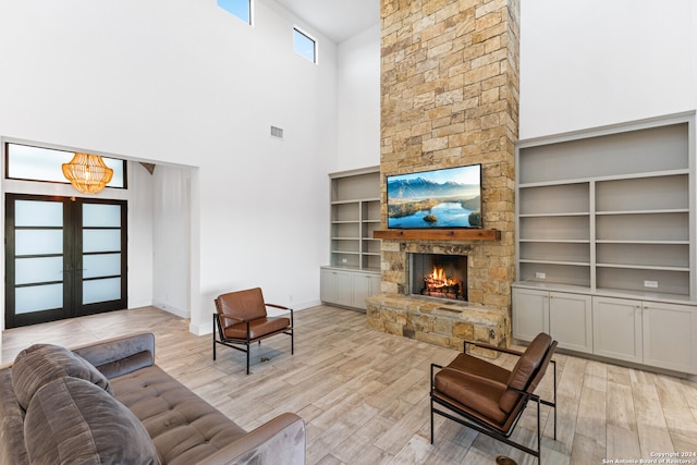 living room featuring light hardwood / wood-style floors, a fireplace, a towering ceiling, and french doors