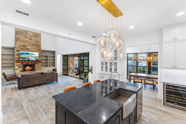 kitchen with a stone fireplace, a kitchen island with sink, wine cooler, and decorative light fixtures