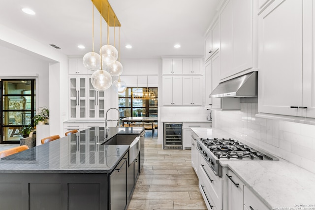 kitchen with a kitchen island with sink, beverage cooler, extractor fan, and light stone counters