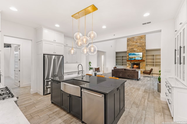 kitchen featuring an island with sink, hanging light fixtures, sink, white cabinetry, and stainless steel appliances