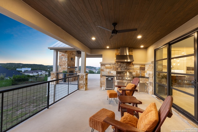 patio terrace at dusk with ceiling fan, grilling area, a balcony, and exterior kitchen