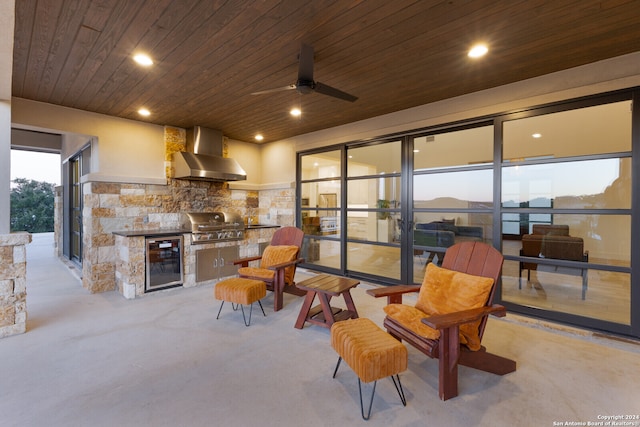 patio terrace at dusk featuring a water view, a grill, beverage cooler, ceiling fan, and exterior kitchen