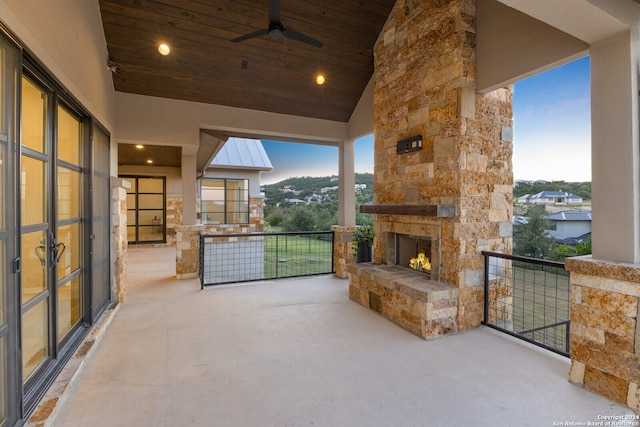 patio terrace at dusk with an outdoor stone fireplace, ceiling fan, and a balcony