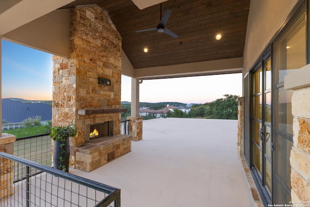 patio terrace at dusk with ceiling fan and an outdoor stone fireplace