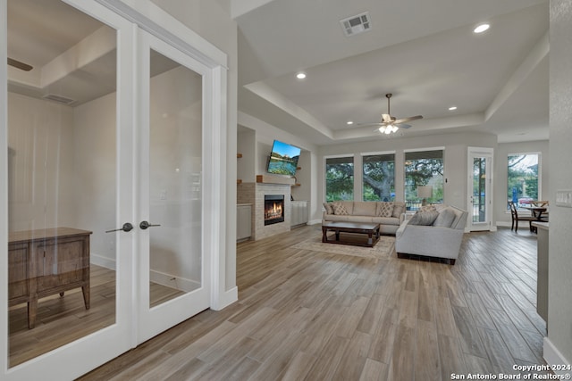 living room featuring french doors, light hardwood / wood-style flooring, a raised ceiling, and ceiling fan