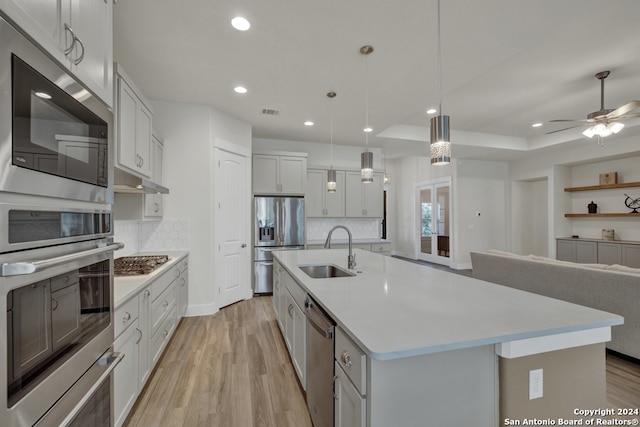 kitchen with pendant lighting, sink, a center island with sink, appliances with stainless steel finishes, and light wood-type flooring