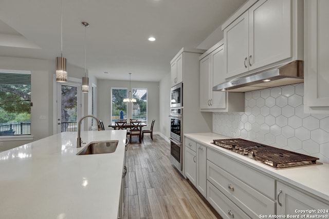 kitchen featuring pendant lighting, light hardwood / wood-style floors, sink, white cabinets, and appliances with stainless steel finishes