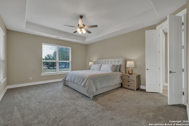 carpeted bedroom featuring a tray ceiling and ceiling fan