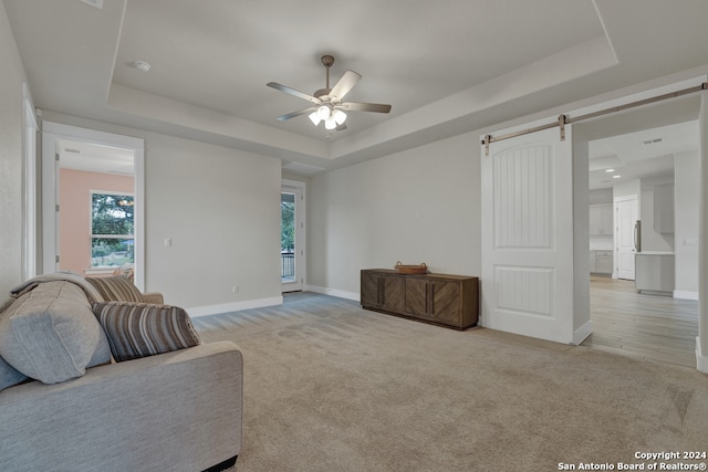 sitting room with a barn door, a tray ceiling, ceiling fan, and light colored carpet