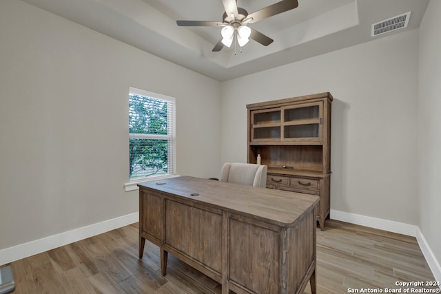 office with light wood-type flooring, a tray ceiling, and ceiling fan