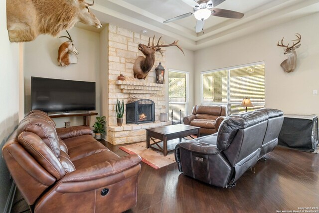 living room with a raised ceiling, a stone fireplace, dark hardwood / wood-style flooring, and ceiling fan