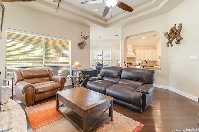 living room with wood-type flooring, ceiling fan with notable chandelier, and a raised ceiling