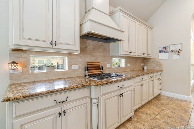 kitchen with stainless steel gas stovetop, premium range hood, vaulted ceiling, and decorative backsplash