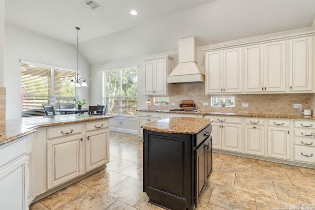 kitchen featuring light stone counters, a center island, lofted ceiling, custom range hood, and backsplash