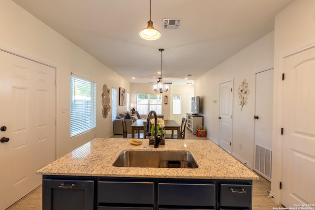 kitchen featuring light stone counters, hanging light fixtures, a kitchen island with sink, and sink