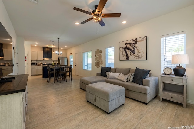 living room featuring ceiling fan with notable chandelier, a wealth of natural light, and light hardwood / wood-style floors