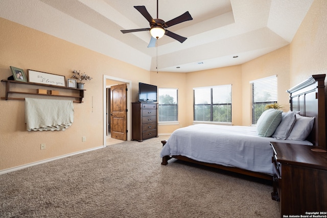 bedroom with light colored carpet, ceiling fan, and a raised ceiling