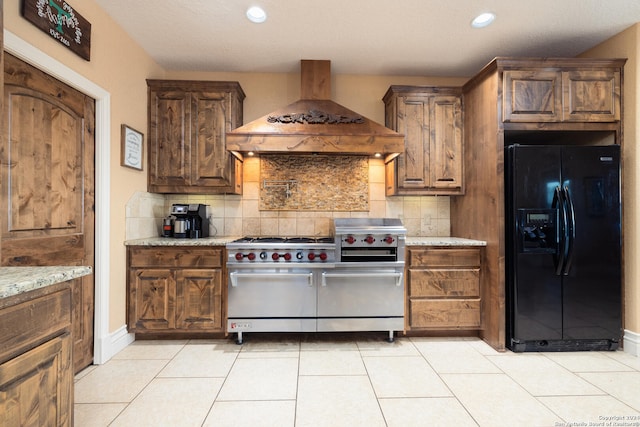 kitchen with light stone counters, luxury range, black fridge with ice dispenser, tasteful backsplash, and wall chimney range hood