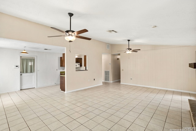 unfurnished living room with ceiling fan, light tile patterned floors, wood walls, and vaulted ceiling