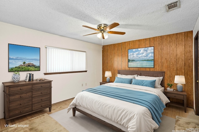 bedroom with light wood-type flooring, wood walls, ceiling fan, and a textured ceiling