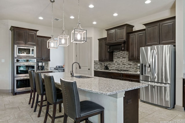 kitchen with an island with sink, appliances with stainless steel finishes, hanging light fixtures, and sink